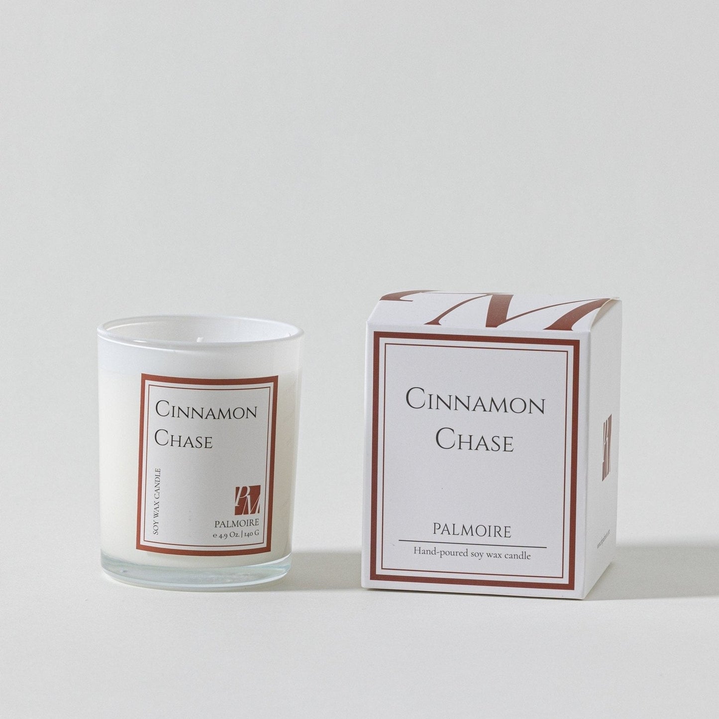 A Cinnamon Chase soy wax candle in a glass jar next to its box.
