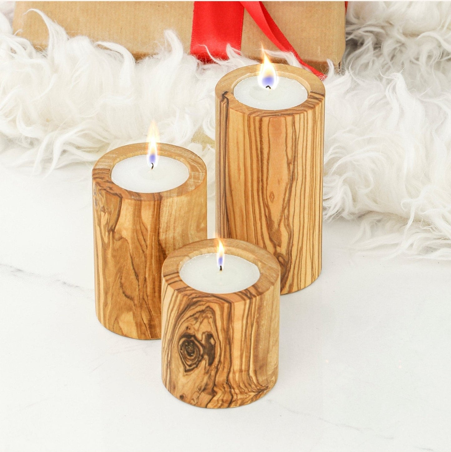Set of three graduated olive wood candle holders with lit candles.