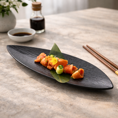 Sushi dish on a black plate with soy sauce and chopsticks on a light wooden table.