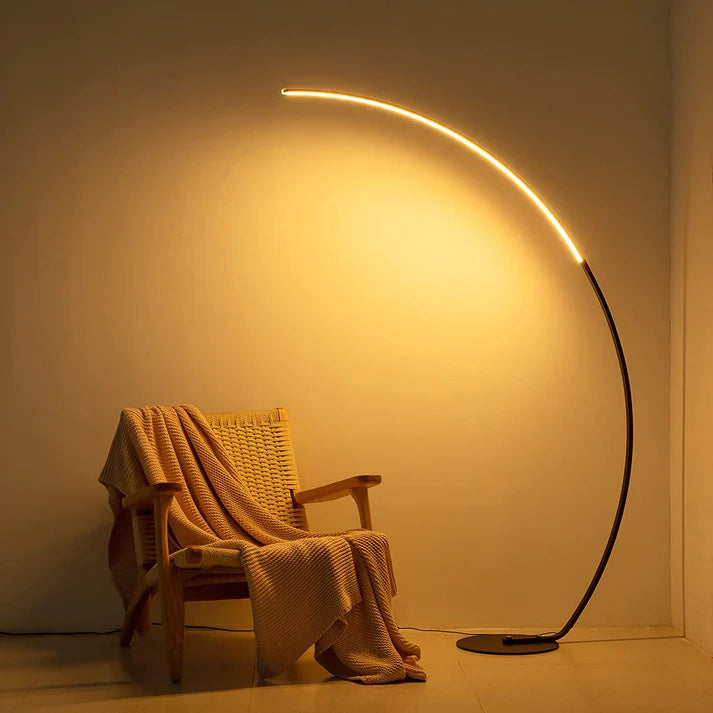 Modern black metal curved LED floor lamp casting a warm glow over a wooden chair with a knit throw.