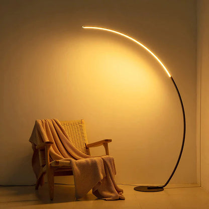 Modern black metal curved LED floor lamp casting a warm glow over a wooden chair with a knit throw.