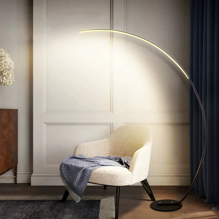 Modern black metal curved LED floor lamp illuminating a beige armchair in a contemporary room.