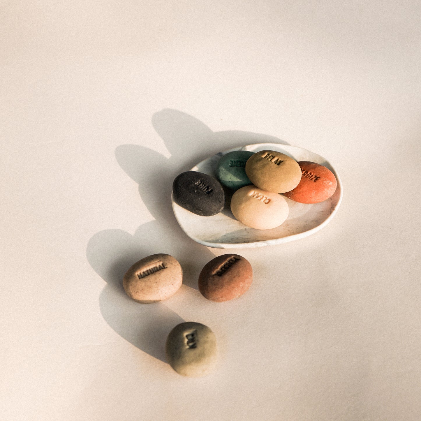 Set of colorful stones on a light surface with a white dish.