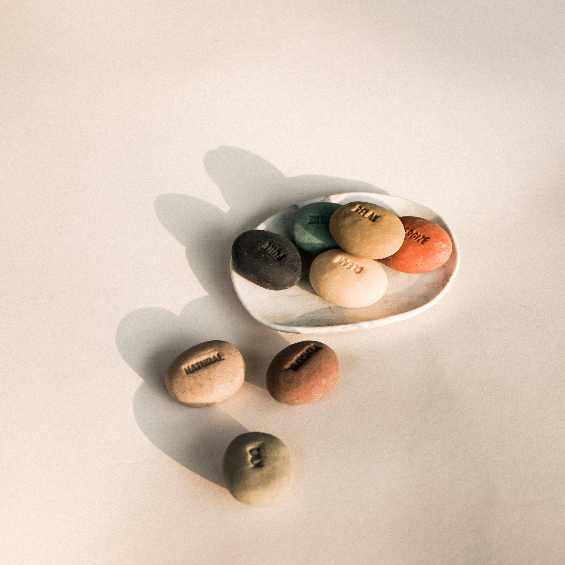 Set of colorful stones on a light surface with a white dish.