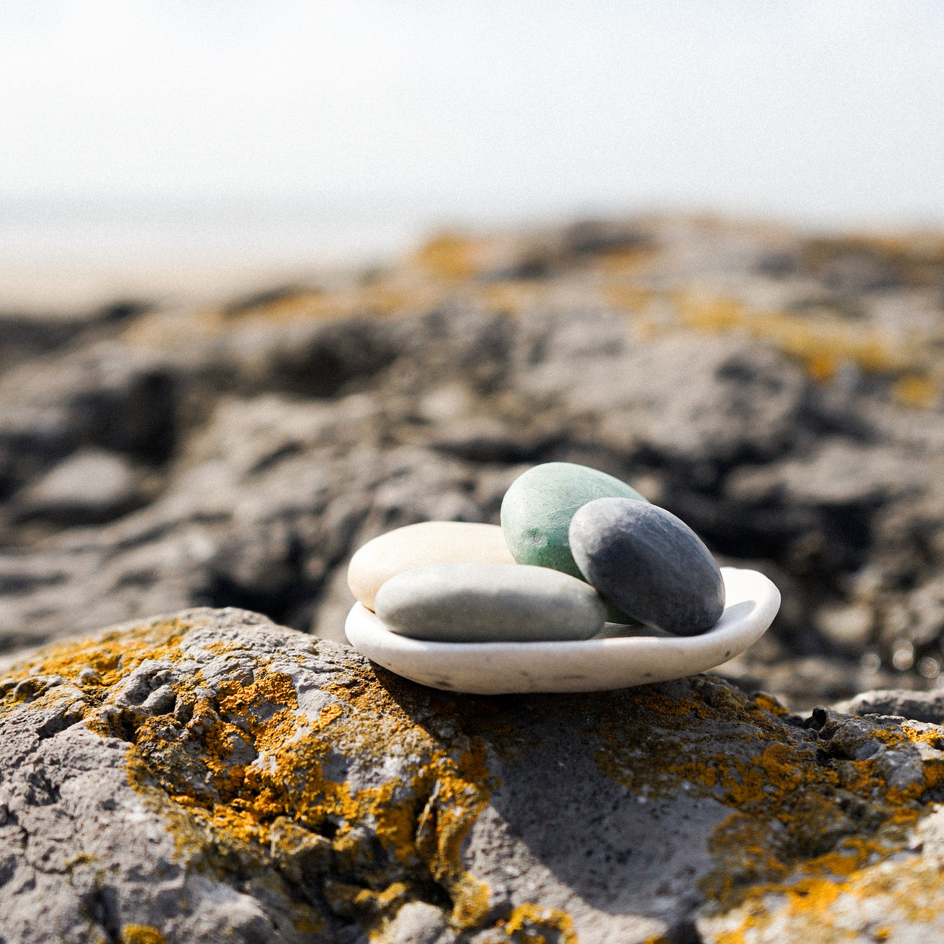 Three stones on a small white dish on a rocky surface with a blurred natural background