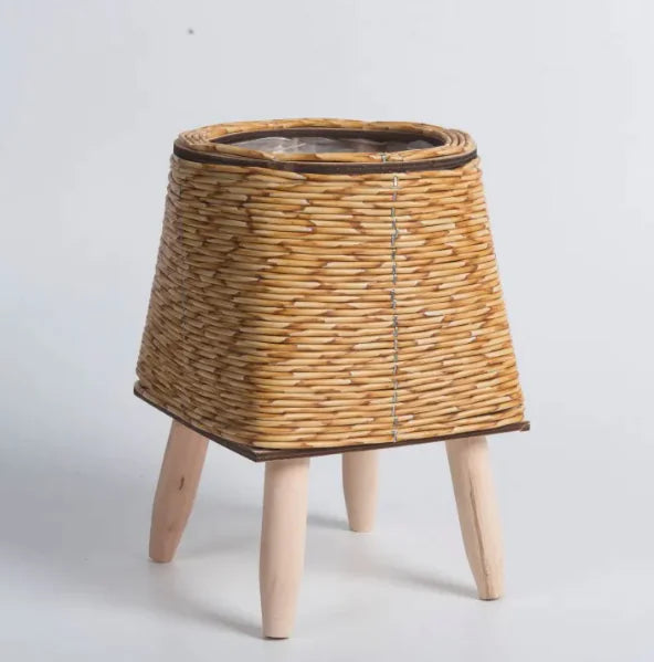 Wicker plant stool with wooden legs on a light gray background