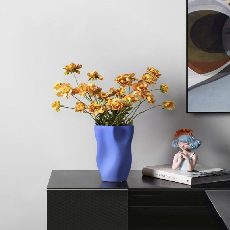 Blue vase with yellow flowers on a black surface next to a framed picture