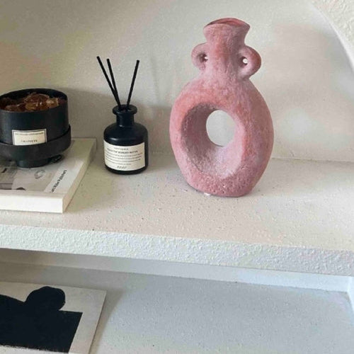 Pink abstract vase on a shelf with decorative items