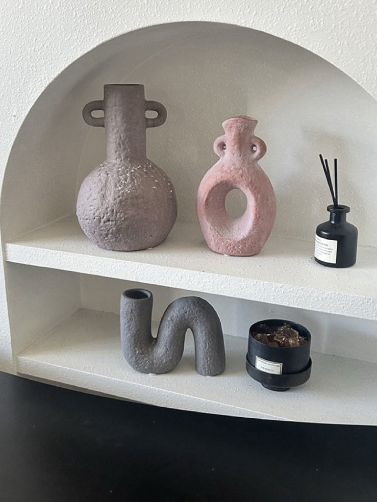 Decorative shelf with various ceramic vases and a diffuser on a plain background