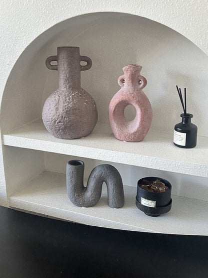 Decorative shelf with various ceramic vases and a diffuser on a plain background