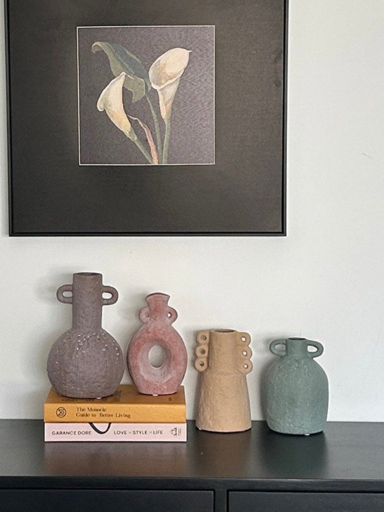 Framed artwork above a shelf with decorative vases and books.