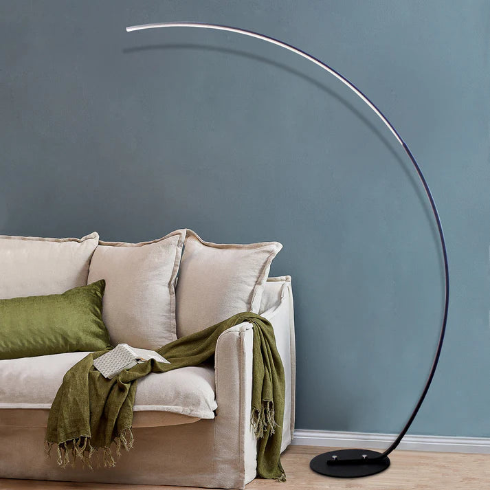 Modern black metal curved LED floor lamp with a weighted base arching over a neutral sofa.