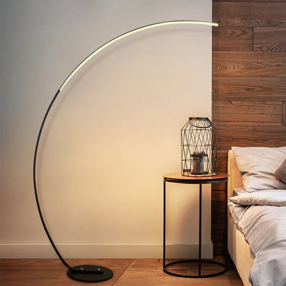 Modern black metal curved LED floor lamp with a weighted base illuminating a bedroom corner.